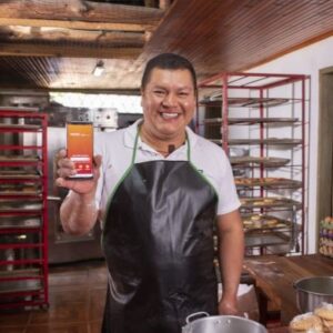 Señor feliz en una panaderia mostrando app Bancamia