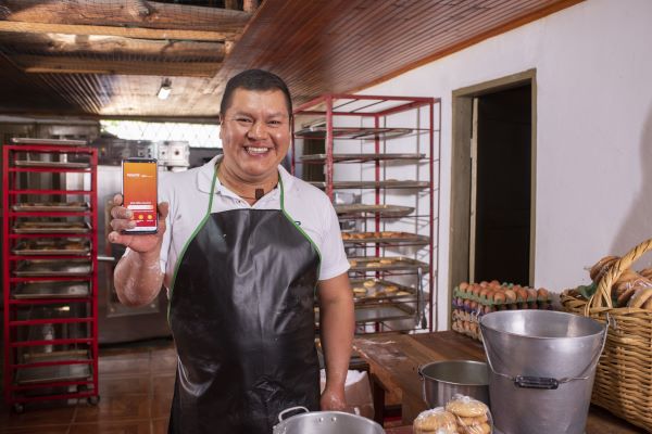 Señor feliz en una panaderia mostrando el celular con la app Bancamia